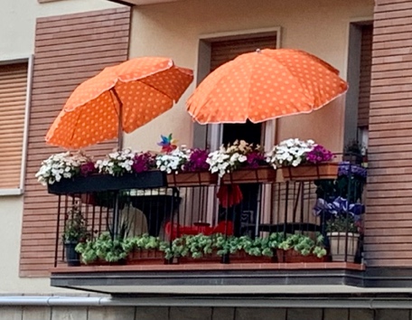 un terrazzo fiorito con due ombrelloni arancioni aperti